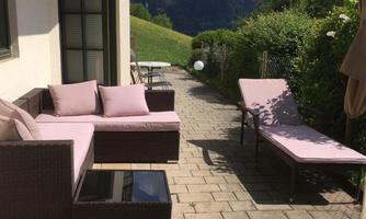 A cozy outdoor area with a sofa and chaise lounges. In the background, gentle hills and mountains are visible.