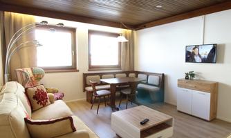 A modern living room with a cozy sofa and a dining table. Large windows allow plenty of daylight in.