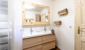A modern bathroom with a double sink and a large mirror. The walls are bright, and wooden shelves with towels create a cozy atmosphere.
