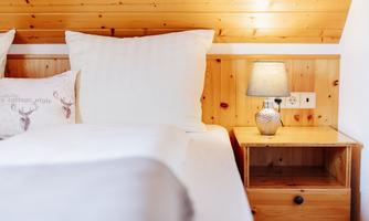 A cozy bedroom with a large bed and white pillows. Next to the bed, there is a nightstand with a lamp and a drawer.