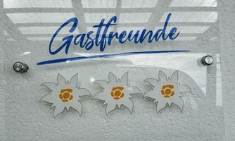 A sign with the word "Guest Friends" in blue lettering. Below are three stylized edelweiss flowers depicted.
