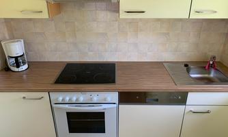 A modern kitchen with a cooktop, an oven, and a sink. Next to the sink is a coffee machine.