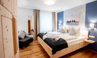 A modern hotel room with a large bed, elegant wooden decor, and natural light. The walls are painted in soft colors, and there are cozy seating areas.