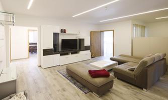 A modern living room with a large TV and comfortable sofas. The room is bright and friendly designed, with wood flooring and minimalist furnishings.
