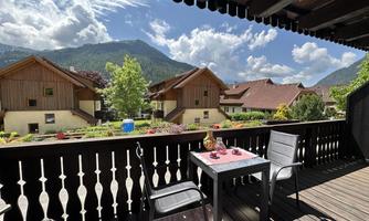 A cozy balcony with a view of mountain houses and a picturesque landscape. The sun is shining and the sky is partly cloudy.