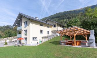 A modern house in the mountains with a beautiful garden. Next to the house is a covered terrace with a barbecue area.