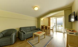 A cozy living room with a sofa, two armchairs, and a table. Large windows offer a view of the outdoors and provide plenty of daylight.