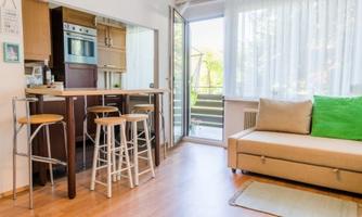 Modern living room with a cozy couch and a small dining area. Large windows provide plenty of daylight and a view outside.