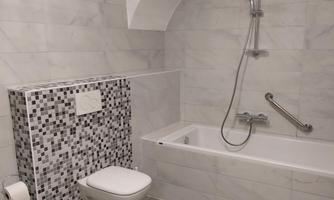 A modern bathroom with a bathtub and a shower. The walls are adorned with light tiles and a decorative mosaic.