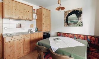 A cozy kitchen with wooden cabinets and a small dining table. A picture of a coastal motif hangs on the wall.