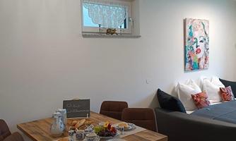 An inviting dining area with a wooden table, set with dishes and sweet treats. In the background, there are cozy seating arrangements and a decorative picture on the wall.
