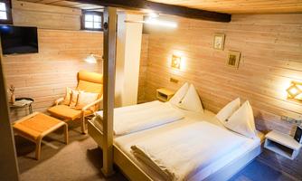 A cozy room with a double bed and wooden walls. There is a television, a seating area, and warm light.