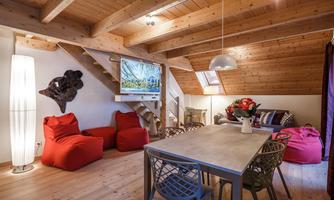 A cozy living area with wooden ceilings and a large dining table. Red bean bags and a modern TV system give the room an inviting atmosphere.