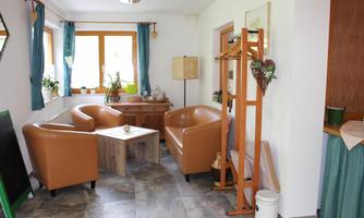 A cozy living space with two brown armchairs and a wooden table.  

There is a coat rack standing against the wall and there are plants on the windowsill.