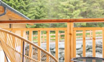 ‘The cosy balcony with its natural wooden railing and stylish outdoor furniture offers an ideal retreat surrounded by nature. A delicate lounge chair and a small side table invite you to relax in the fresh mountain air and let your gaze wander over the surrounding green forests. The warm wood look blends harmoniously into the natural surroundings and creates a calm, relaxing atmosphere.’