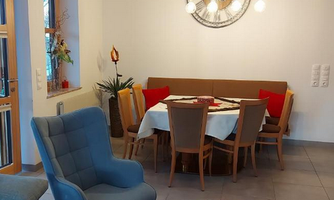 An inviting dining area with a round table and chairs. The cozy bench is decorated with colorful cushions and there is modern lighting.