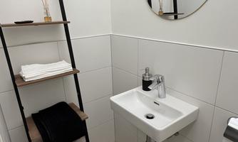 A modern bathroom with elegant tiles and a small sink. On the wall, there is a practical shelf with towels and decorations.