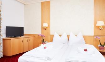 A cozy room with two beds and modern wooden furniture. A television is hanging on the wall and there are decorative flowers on the bedside table.
