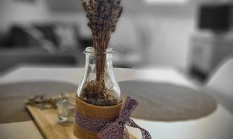 A decorative glass vase with dried lavender flowers sits on a wooden tray. The vase is adorned with a ribbon and adds a cozy atmosphere to the room.