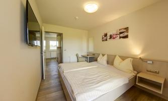 A cozy hotel room with a double bed and neutral colors. There is a television, a table, and artworks on the wall.