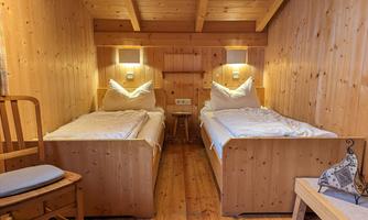 A cozy room with two wooden single beds. The walls are also made of wood, and there is warm lighting.