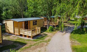 Pretty wooden lodgings in a green environment. The path leads through a quiet campsite with trees.