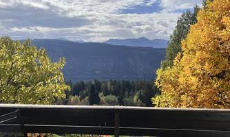 A view from a balcony of a picturesque mountain landscape with colorful autumn trees. The sky is partly cloudy and provides a beautiful contrast to nature.