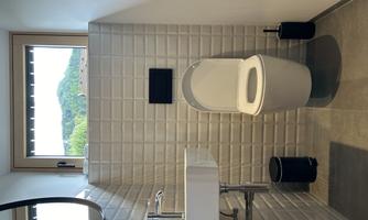 A modern bathroom with a white toilet and a sink. Through the window, you can see the green mountains outside.