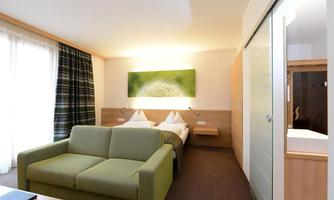 A modern room with two beds and a green sofa. Large windows provide plenty of light and a relaxed atmosphere.