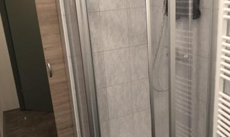 A modern shower with glass partition in a bright bathroom. The walls are tiled and there is a radiator next to the shower.
