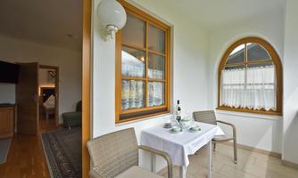 A cozy balcony with two chairs and a table, decorated with glasses and a bottle of wine. Plenty of daylight is visible through the windows, creating an inviting atmosphere.