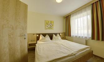 A cozy bedroom with a double bed and two pillows. Curtains in colorful stripes and a window with daylight complement the room.