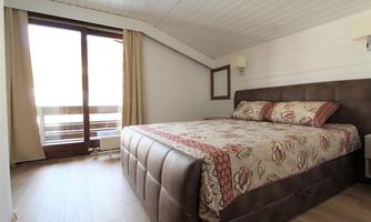 A cozy bedroom with a large bed and a balcony.  
Bright walls and natural light sources create an inviting atmosphere.