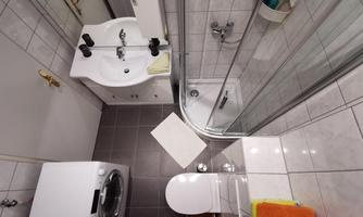 A modern bathroom with a shower, sink, and toilet. A white mat is on the floor and a washing machine is in the corner.
