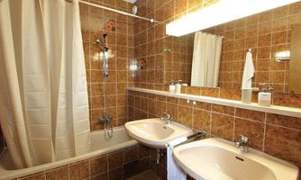 A bathroom with brown tiles, a bathtub, and two sinks. There is also a shower curtain and a mirror.