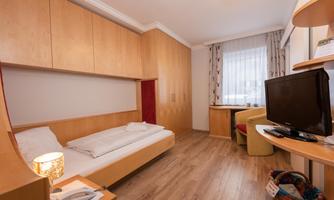 A simple room with wooden shelves and a single bed. The room is bright and has a window with curtains.