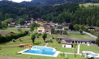 A beautiful swimming pool surrounded by green meadows and trees. In the background are picturesque houses and mountains.