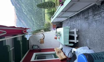 A cozy balcony with a table and chairs. In the background, green mountains and forests can be seen.