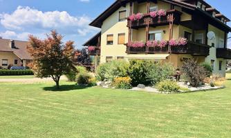 A beautiful house with colorful flower balconies and a well-maintained garden. The sky is clear and blue, creating a relaxed atmosphere.