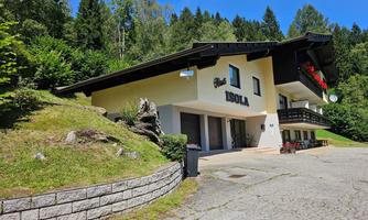 A friendly building in the mountains under a clear blue sky. Surrounded by trees and greenery, it offers an inviting atmosphere.