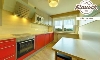 A modern kitchen with red cabinets and a large window. The space is bright and inviting.