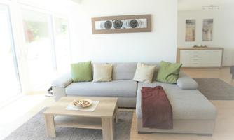 A stylishly furnished living room with a gray sofa and green cushions. The room is bright and inviting, with a table and decorative elements.