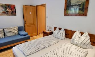 A cozy bedroom with two beds and white pillows. It also has a seating area with a blue sofa and a wooden wardrobe.