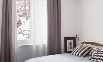 A modern bedroom with a cozy bed and striped pillows. Bright curtains let in plenty of natural light.