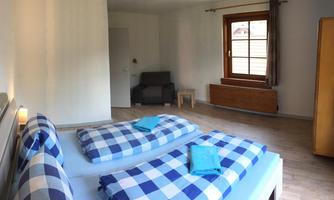 A simple, bright room with two beds and checked bedspreads. The room has a window overlooking the outside and some furniture pieces.
