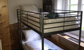 A simple room with a bunk bed and a small table. The window lets in plenty of daylight.