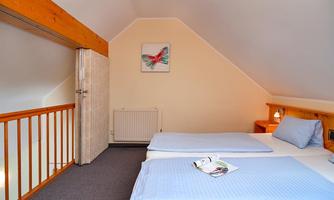 A cozy bedroom with two beds and blue bedspreads. The wall is painted light and a picture of a butterfly hangs above it.
