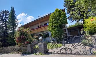 An impressive house with a beautiful garden and tall trees. The sky is clear and sunny.