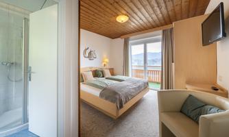 A cozy bedroom with a double bed and a small balcony. The room has a wooden ceiling, a television, and a connection to a bathroom.