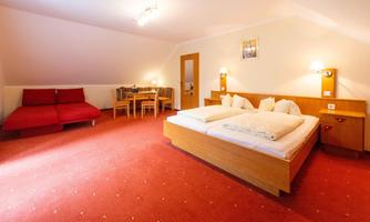 A spacious hotel room with a double bed, a table and chairs, as well as a comfortable sofa. The warm colors and gentle lighting create an inviting atmosphere.